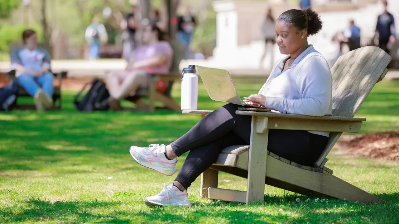 girl sitting in a chair on the quad with her laptop and water bottle