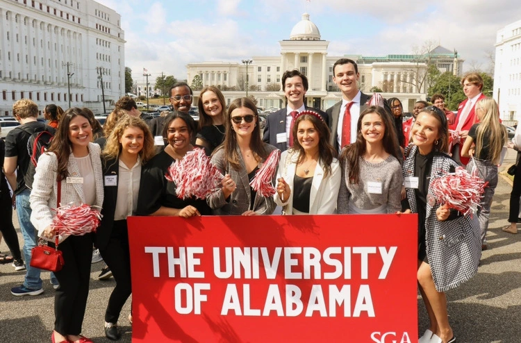 nick poses for a photo with a group of blackburn students while the alabama state capitol building sits in the background