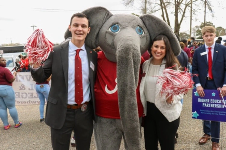 nick poses with big al and a female peer while waving a pom-pom 