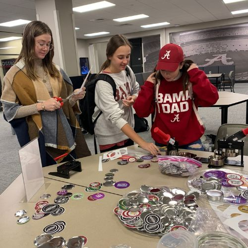 three students stand around a table and peruse through items available for them to use for their student organization