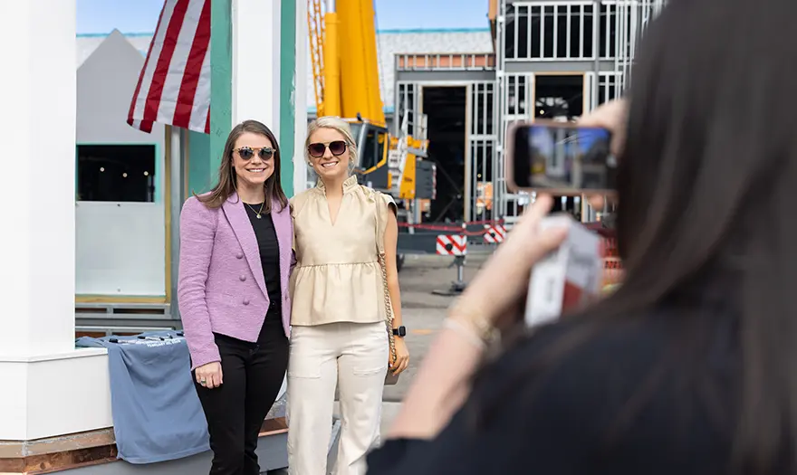 Two women smiling for a photo in front of the cupola while another person takes their picture.