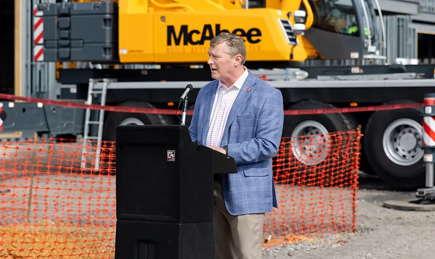 Dr. Hood speaks at a podium during the Well-being Hub's topping out ceremony.
