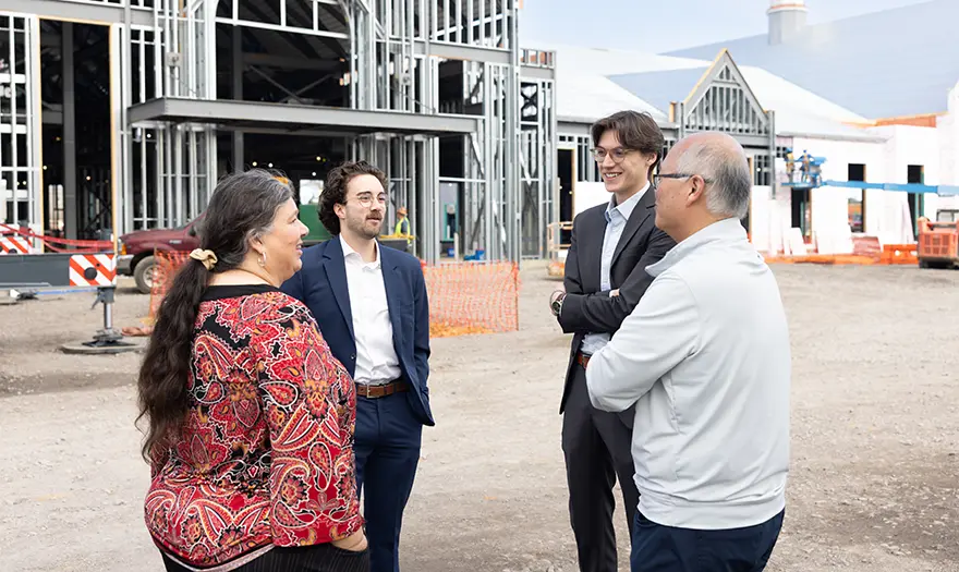 Four individuals chatting with the newly constructed Well-being hub seen behind them.