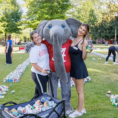 Two students pose on either side of Big Al holding soup cans