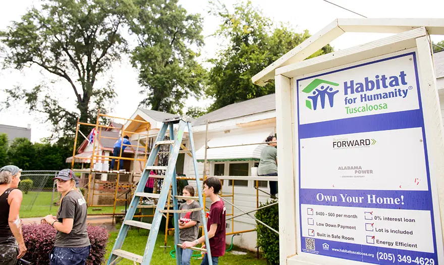 Students work on a house next to a Habitat for Humanity sign.
